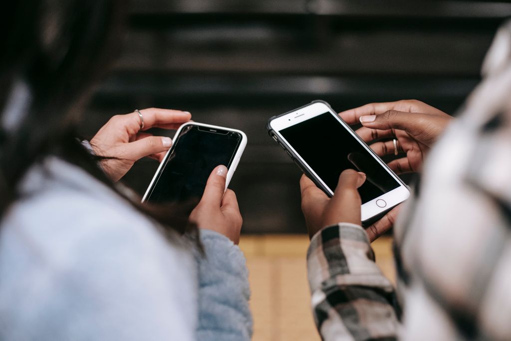 Back view of crop anonymous black woman touching screen of cellphone near girlfriend watching gadget while spending time together