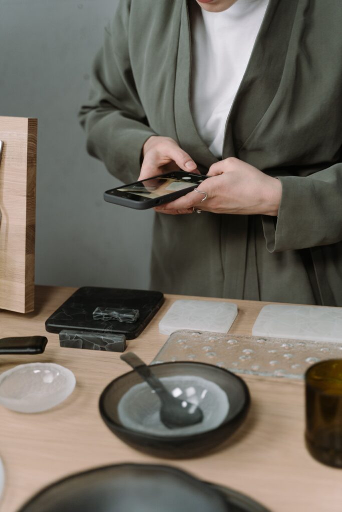 A person photographing handcrafted ceramics on a table using a smartphone.
