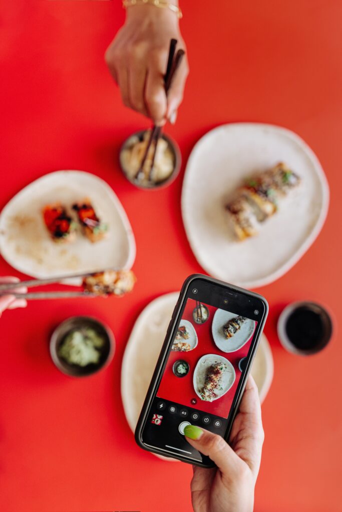 A smartphone captures a vibrant sushi dinner with chopsticks and a bold red background.
