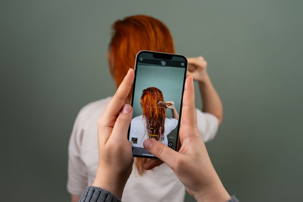 Photographing a person with red hair using a smartphone indoors.